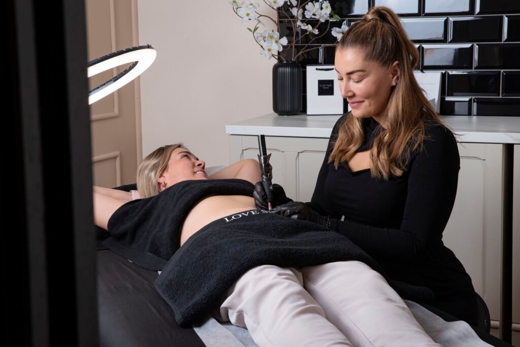 female cosmetic tattoo artist using tattoo gun on clients abdomen