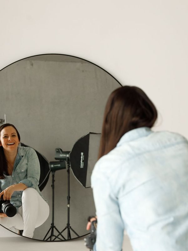 Photographer looking into a mirror smiling while holding a camera